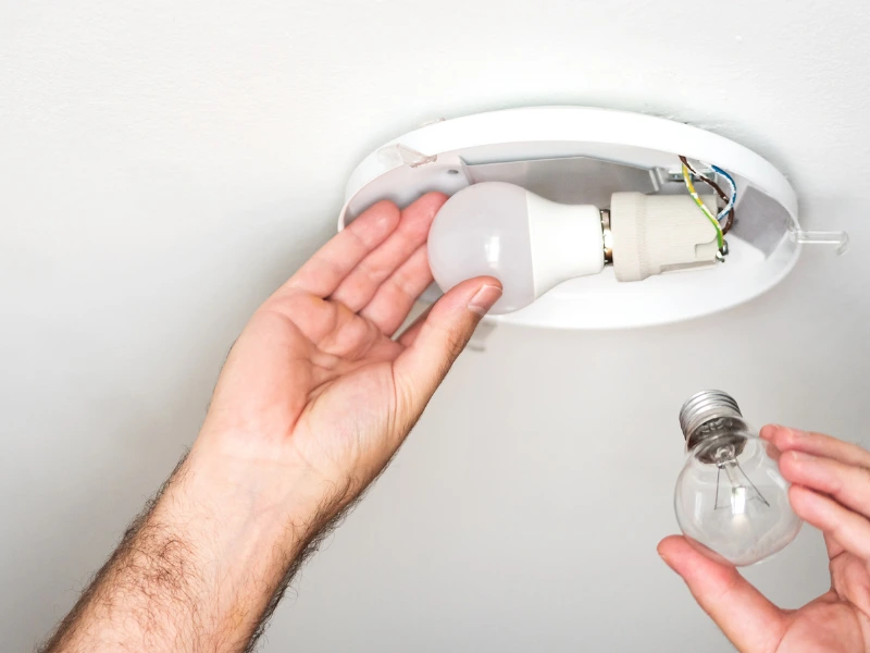 man replacing old incandescent light bulb with new led light.